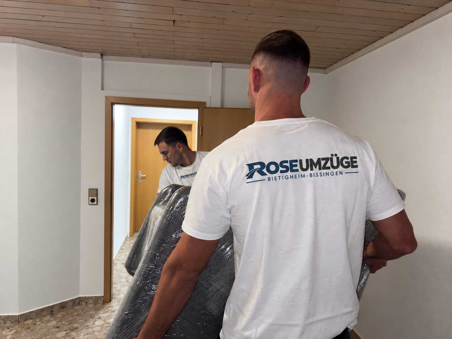 Umzugshelfer von Rose Umzüge tragen eine eingepackte Couch bei einem Umzug in Bietigheim-Bissingen